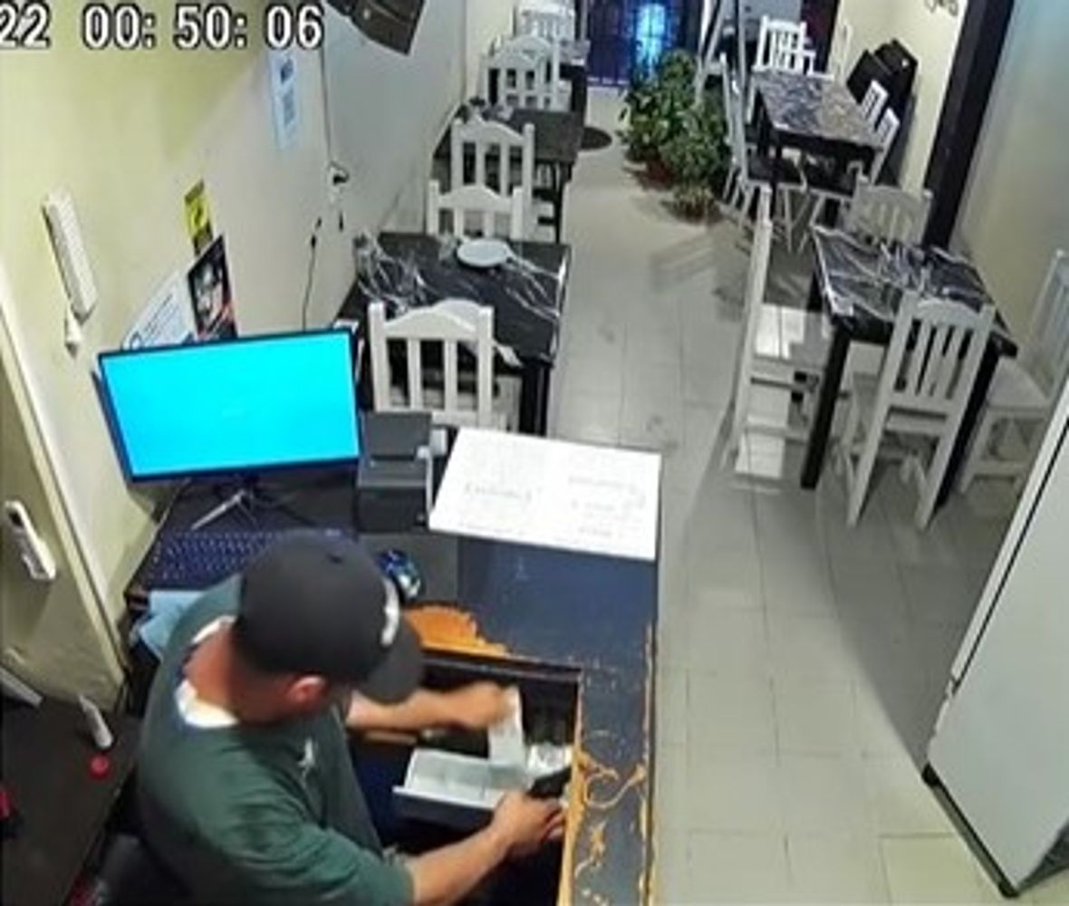 Con el arma en la mano derecha, el asaltante saquea la caja registradora, aprovechando la ausencia de clientes en el local gastronómico.