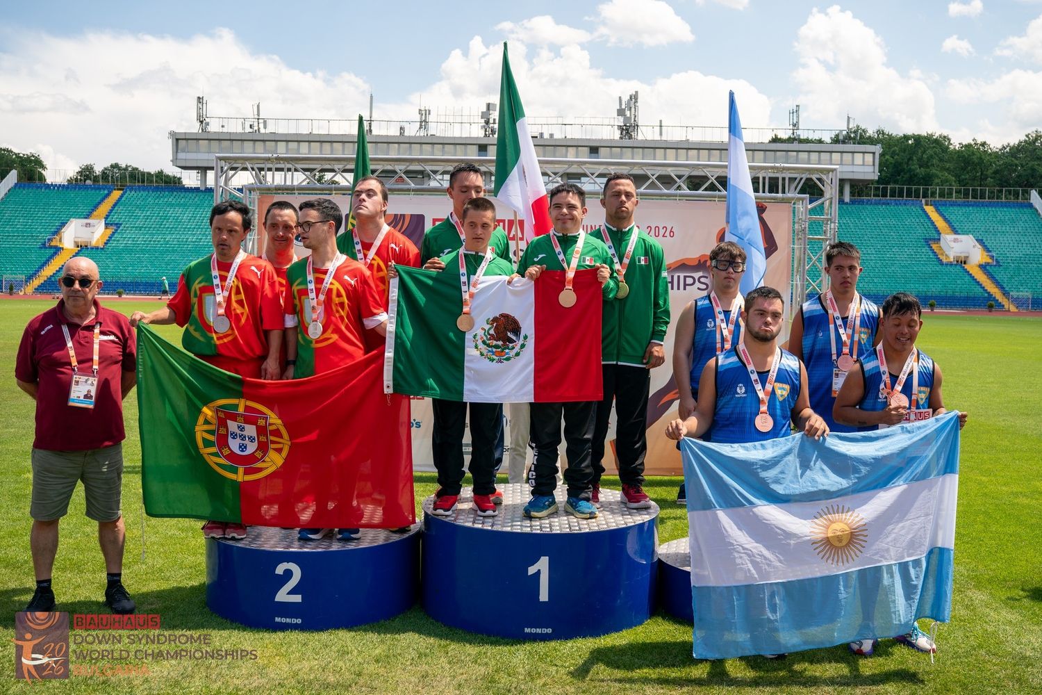 El tercer mejor equipo del mundo en la prueba de relevos, en el Mundial de Bulgaria: el sampedreño Carlos Isasmendi (a la derecha) en el podio sosteniendo con orgullo la Bandera argentina.