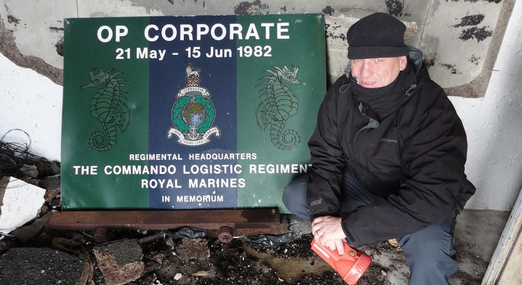 Thomas, en 2012 de regreso a las Malvinas, en el 30° aniversario de la guerra. junto a una placa conmemorativa en el Red & Green Life Machine Field Hospital (el hospital de campaña en el que trabajó después del trágico suceso del 8 de junio). El lugar, un antiguo frigorífico, permanece en ruinas.                        