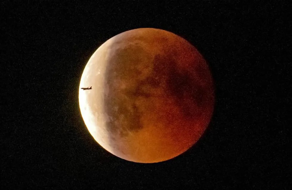 An airplane passes the blood moon immediately after the total lunar eclipse in Erfurt, Germany, Friday, July 27, 2018. Skywatchers around much of the world are looking forward to a complete lunar eclipse that will be the longest this century. (AP Photo/Jens Meyer)
