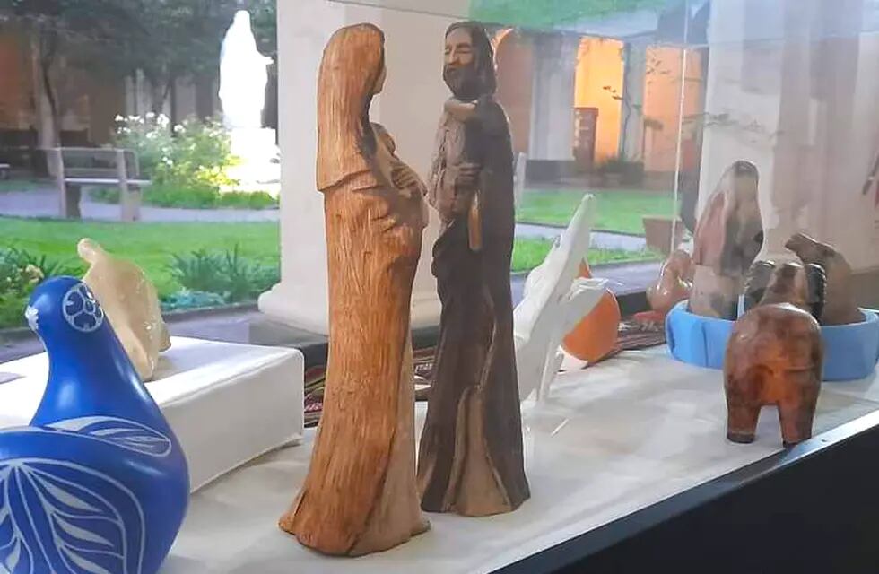 Estilizadas imágenes talladas en madera que representan a María y José, junto a figuras de diversos estilos y diferentes materiales, en la muestra montada en los jardines del convento franciscano de Jujuy.