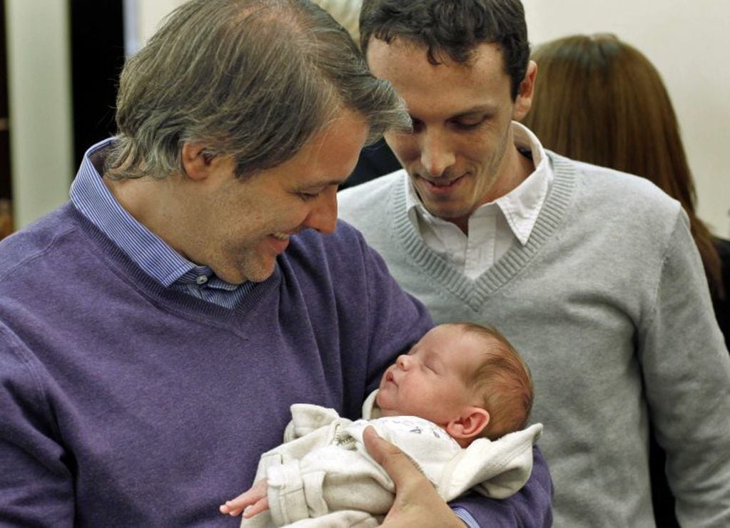 Alejandro Grinblat y Carlos Dermger sonríen junto a su hijo Tobías, en 2012, en un Registro Civil de Buenos Aires (Argentina). Tobías, un bebé de tres semanas nacido de una madre de alquiler en la India (Foto: EFE/Leo La Valle)