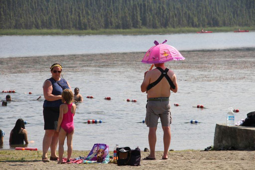 Un hombre se cubre del sol junto a su hijo en brazos con una sombrilla en "Goose Lake" en Anchorage, Alaska. Foto: AP, Mark Thiessen.