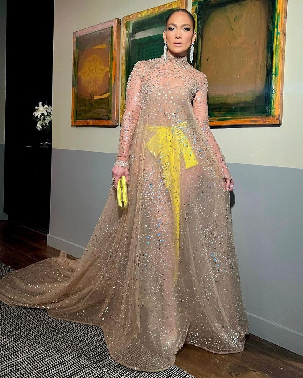 Jennifer López en vestido de gala con transparencia a juego con bolso y lazo en amarillo satín