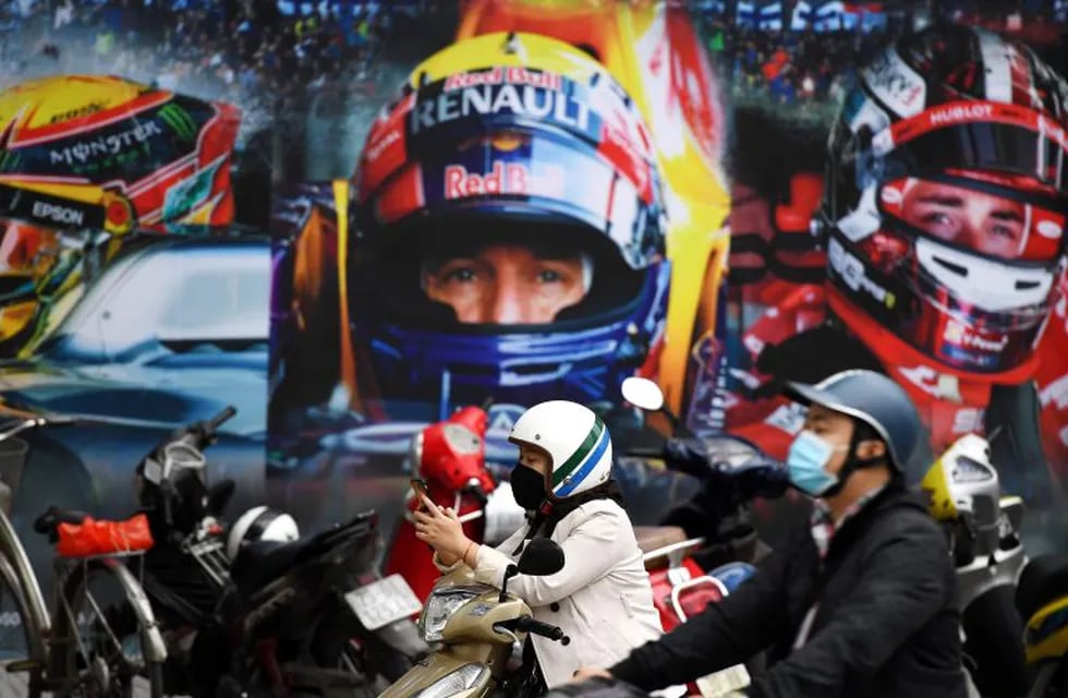 (FILES) In this file photo taken on March 2, 2020 a woman wearing a facemask checks her smartphone in front of a poster outside the Formula One Vietnam Grand Prix merchandise store in Hanoi. - Vietnam's 2020 Formula One Grand Prix has been cancelled, organisers said on October 16, but there was no word on whether the race would take place next year. (Photo by Nhac NGUYEN / AFP)