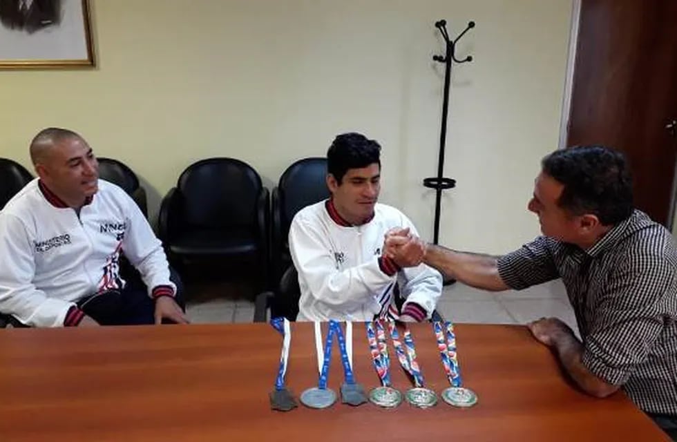 Hugo Piriz con sus medallas logradas en los Juegos Evita, junto a su entrenador el profesor Bonastre, saludado por el ministro de Salud de Misiones, Walter Villalba. /Ministerio de Salud de Misiones, prensa)