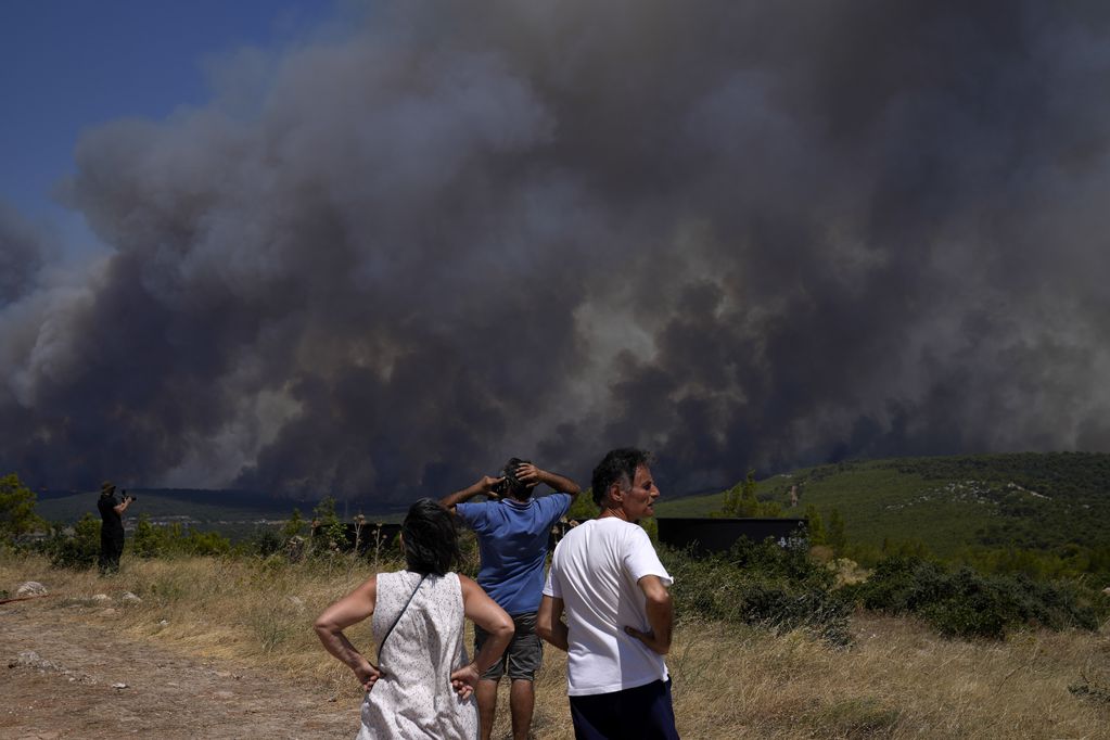 Vecinos observan un incendio en una ladera desde la aldea de Pournari, cerca de Atenas, martes 18 de julio de 2023. Tres grandes incendios ardían en las afueras de Atenas y se pronostica una nueva ola de calor para el jueves. (AP Foto/Thanassis Stavrakis)