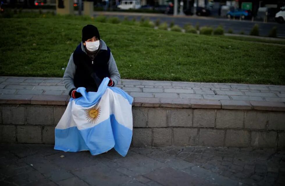A woman, holding an Argentine national flag, sits on a stone ledge wall during a protest against a wide range of issues including government economic policy and state policies to combat the spread of COVID-19, in Buenos Aires, Argentina, Saturday, Sept. 19, 2020. (AP Photo/Natacha Pisarenko)