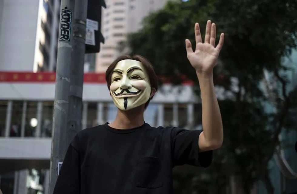 A demonstrator wearing an 'anonymous mask', also known as a Guy Fawkes mask, raises his hand during a protest in the Central district of Hong Kong, China, on Friday, Oct. 4, 2019. Hong Kong invoked emergency powers for the first time in more than half a century to ban face masks for protesters after months of unrest, prompting demonstrators to occupy downtown streets. Photographer: Chan Long Hei/Bloomberg