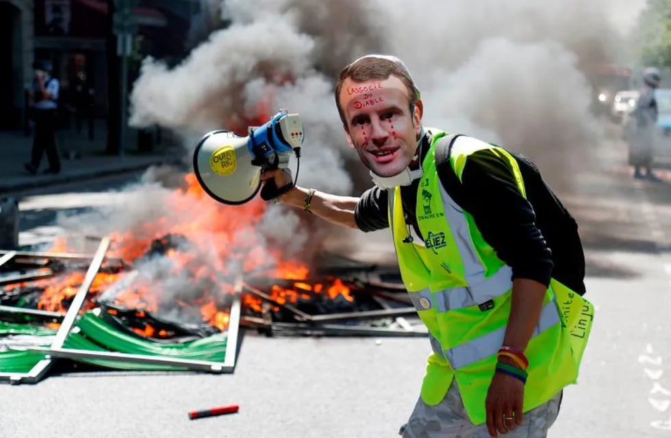 TOPSHOT - A protester wearing a mask of French President Emmanuel Macron crying stands next to a burning barricade during an anti-government demonstration called by the 'Yellow Vests' (gilets jaunes) movement, on April 20, 2019 in Paris. (Photo by Zakaria ABDELKAFI / AFP)