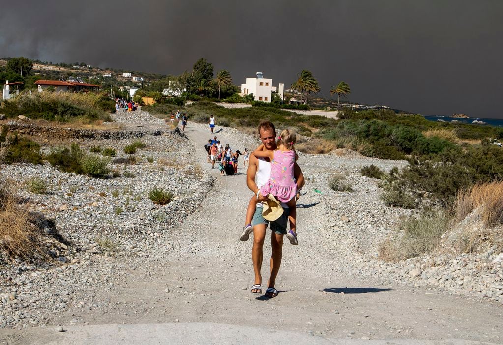 Un hombres lleva a una niña al abandonar la zona donde arde un incendio forestal en la isla de Rodas, Grecia, el sábado 22 de julio de 2023. (Lefteris Diamanidis/InTime News via AP)