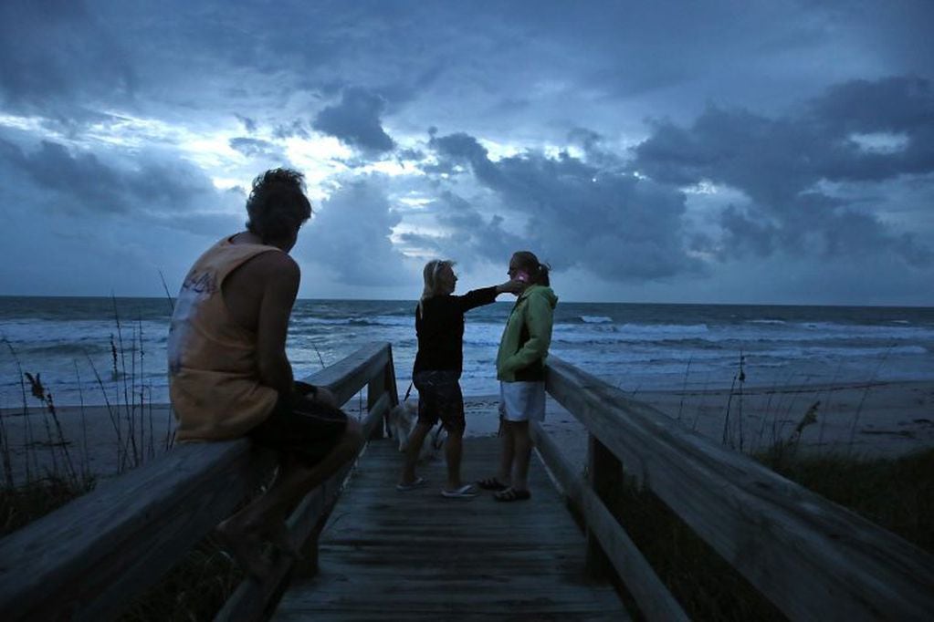 SATELLITE BEACH, FL - OCTOBER 06: Colleen Ydo (C) reaches to hug neighbor Karen Smith (R), as her husband Rod Smith (L), sits nearby on October 6, 2016 on Satellite Beach, Florida. Hurricane Matthew is expected to reach the area later this afternoon.   Ma