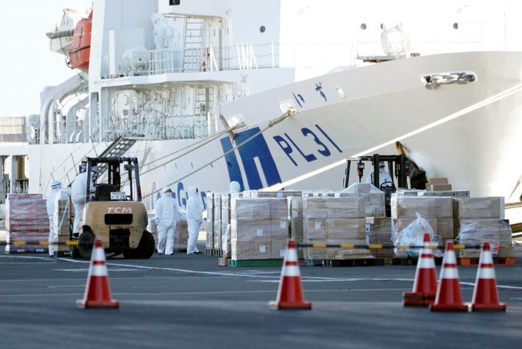 Trabajadores correctamente protegidos cargan víveres en el barco que se encuentra en cuarentena (EFE)