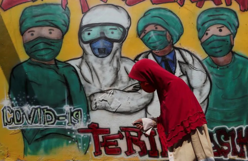 A woman wears a face mask to help curb the spread of the new coronavirus past a coronavirus awareness mural at Rawa Pasung village in Bekasi on the outskirts of Jakarta, Indonesia, Thursday, July 23, 2020. (AP Photo/Achmad Ibrahim)