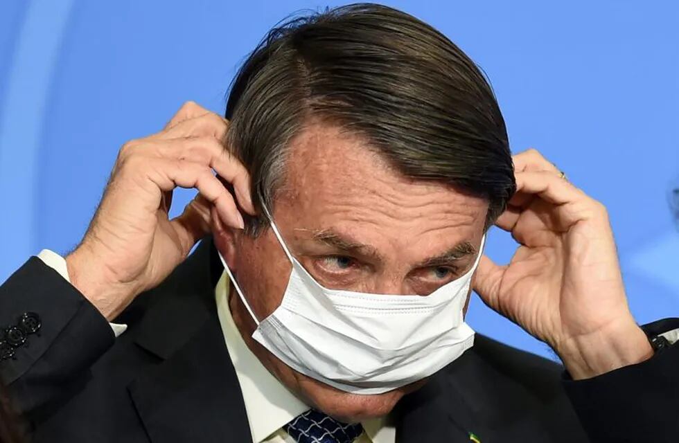 Brazilian President Jair Bolsonaro puts on a facemask during the signing ceremony of a new decree that facilitates access to credit for small business and fights the economic impacts resulting from the pandemic of the novel coronavirus, at Planalto Palace in Brasilia, on August 19, 2020. (Photo by EVARISTO SA / AFP)