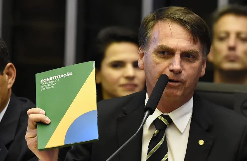 (FILES) In this file photo taken on November 06, 2018 Brazilian far-right president-elect, Jair Bolsonaro (R), holds a constitution beside his vice president Hamilton Mourao during the ceremony celebrating the 30th anniversary of the Brazilian constitution in the National Congress in Brasilia. - Brazil's next president, Jair Bolsonaro, takes office on January 1, 2019 with promises to radically change the path taken by Latin America's biggest country by trashing decades of center-left policies. But while the far-right politician enjoys sky-high popularity of 75 percent going into the top job, the challenges to his agenda are formidable. (Photo by EVARISTO SA / EVARISTO SA / AFP)