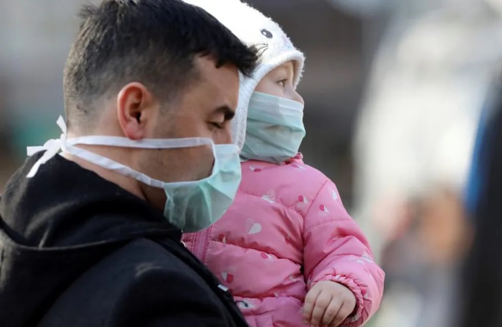 A man holds a baby while walking by the entrance of Zekai Tahir Burak Hospital where 17 passengers of a Turkish Airlines flight from Tehran, suspected of having coronavirus, were to be quarantined, in Ankara, Turkey, Tuesday, Feb. 25, 2020. All 132 passengers of Tehran-Istanbul flight and crew on board will be quarantined for 14 days at the same hospital where Turkish citizens returning from China had been quarantined.( AP Photo/Burhan Ozbilici)