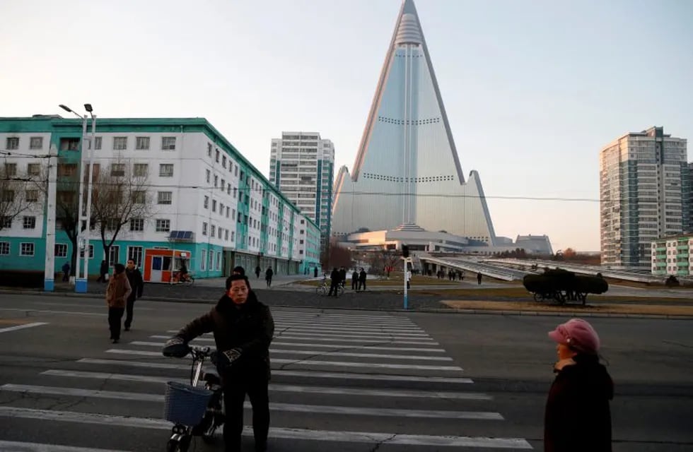 People cross a road as the pyramid-shaped Ryugyong Hotel building looms in the background in Pyongyang, North Korea, Thursday, Dec. 20, 2018. Construction on the hotel, the capital city's most conspicuous landmark, began in 1987 but the work has not been completed and it has never hosted any guests. It is believed to be the tallest unfinished building in the world. (AP Photo/Dita Alangkara)