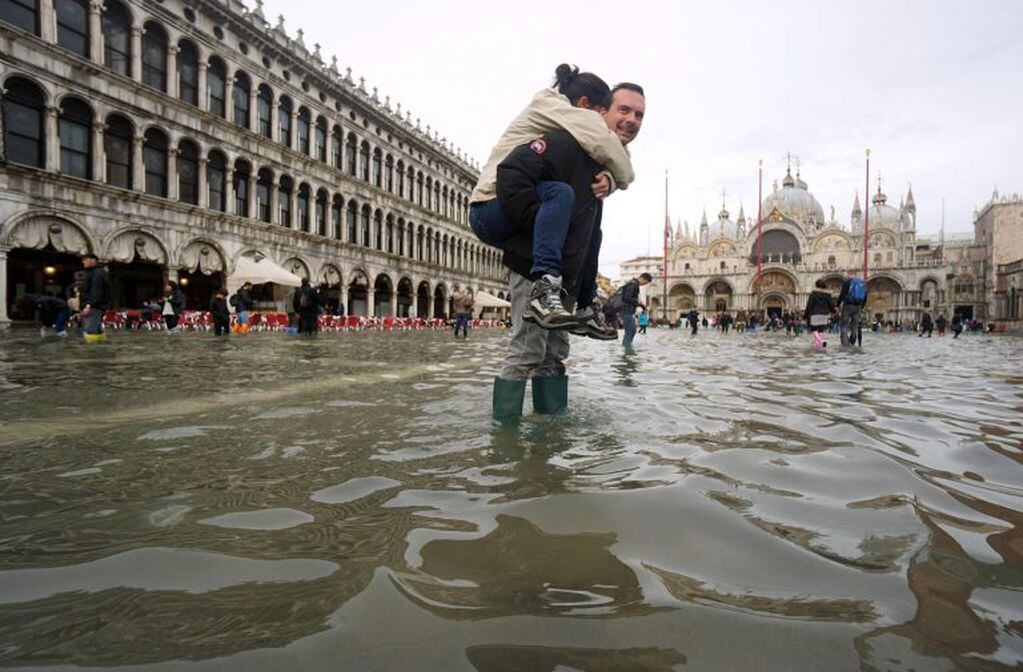 Un hombre carga a sus espaldas con su hija en la Plaza de San Marco, Venecia, inundada (Foto: EFE/ Andrea Merola)