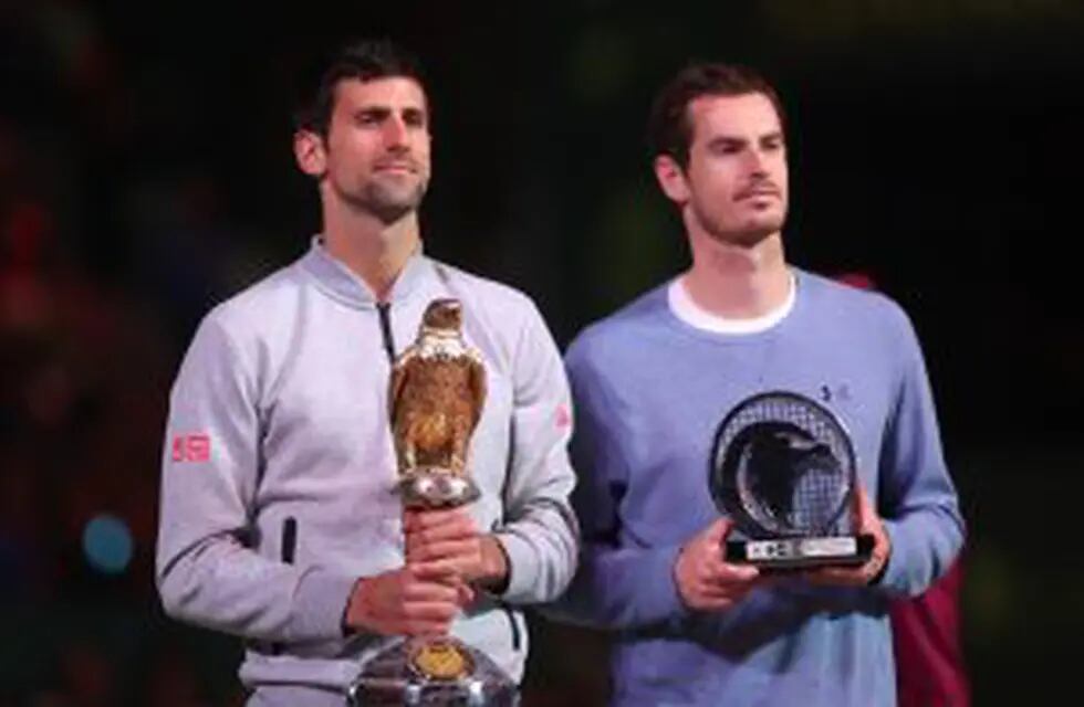 Serbia's Novak Djokovic (L) poses with the winner's trophy after beating Britain's Andy Murray during their final tennis match at the ATP Qatar Open in Doha on January 7, 2017. / AFP PHOTO / KARIM JAAFAR
