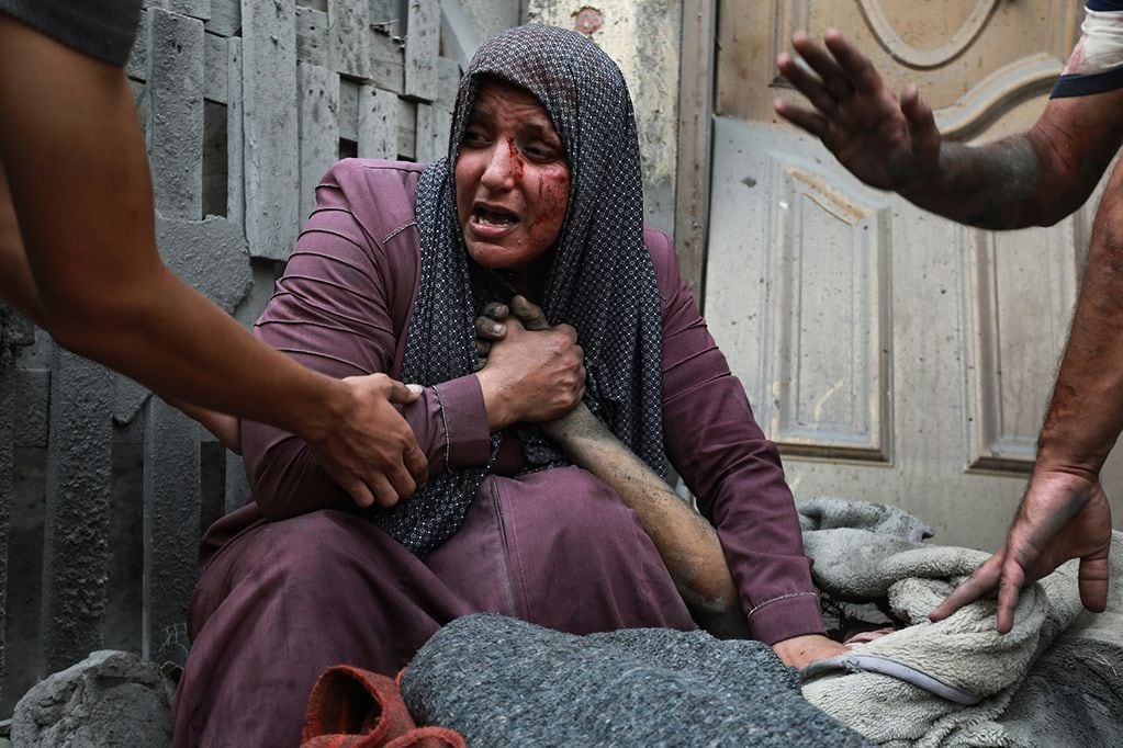 Una mujer palestina herida llora mientras sostiene la mano de su pariente muerto afuera de su casa luego de los ataques aéreos israelíes.