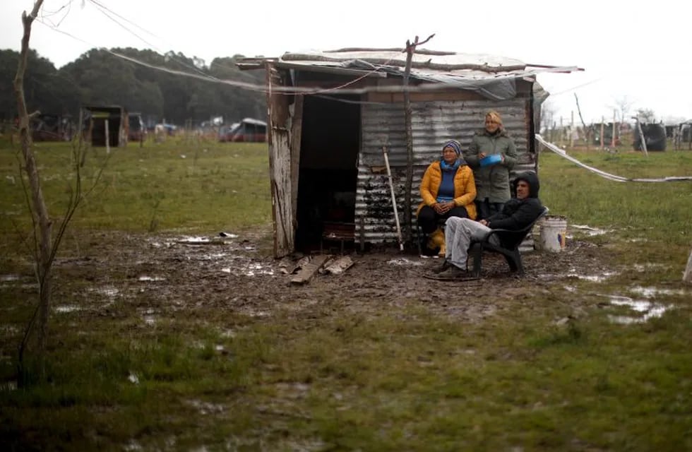A family sits outside a makeshift home at a squatters camp in Guernica, Buenos Aires province, Argentina, Sunday, Sept. 27, 2020. A court has ordered the eviction of families who are squatting there since July, but the families say they have nowhere to go amid the COVID-19 pandemic. (AP Photo/Natacha Pisarenko)
