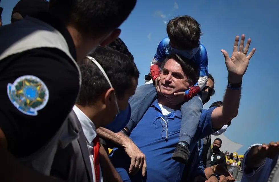 Brazil's President Jair Bolsonaro carries a boy on his back as he greets supporters gathered outside the presidential palace in Brasilia, Brazil, Sunday, May 31, 2020. (AP Photo/Andre Borges)