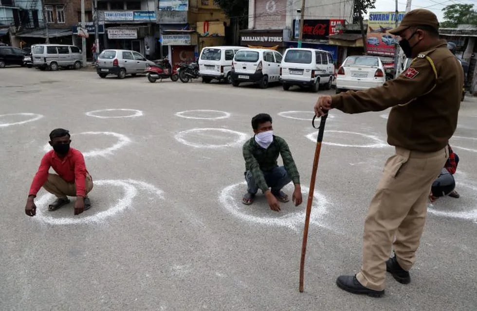 En la ciudad de Jammu, un policía obliga a dos ciudadanos a permanecer en cuclillas, como castigo por romper la cuarentena. (Jaipal Singgh/EFE).