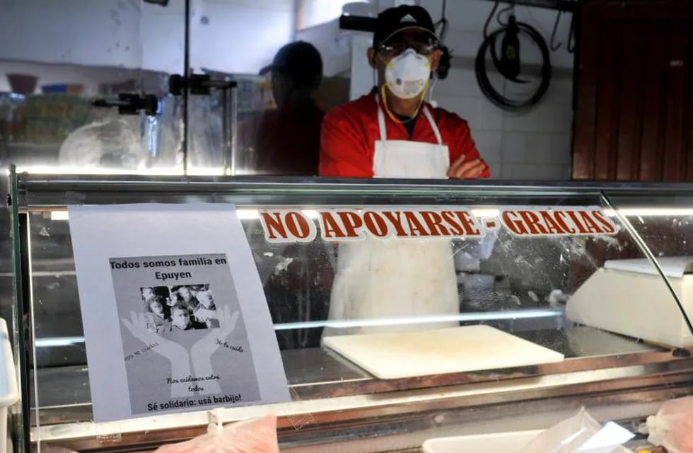 A man wearing a mask waits for clients at his shop, with a sign posted that reads in Spanish \