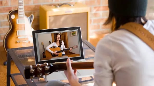Mujer tocando la guitarra frente a la pantalla.