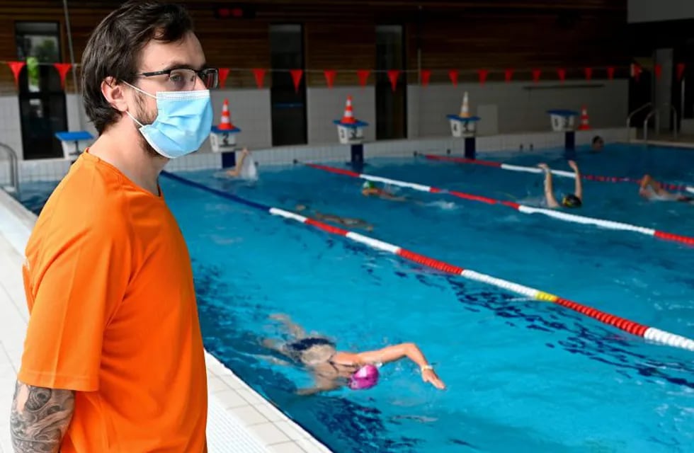 A lifeguard wearing a protective face mask monitors people swimming in \