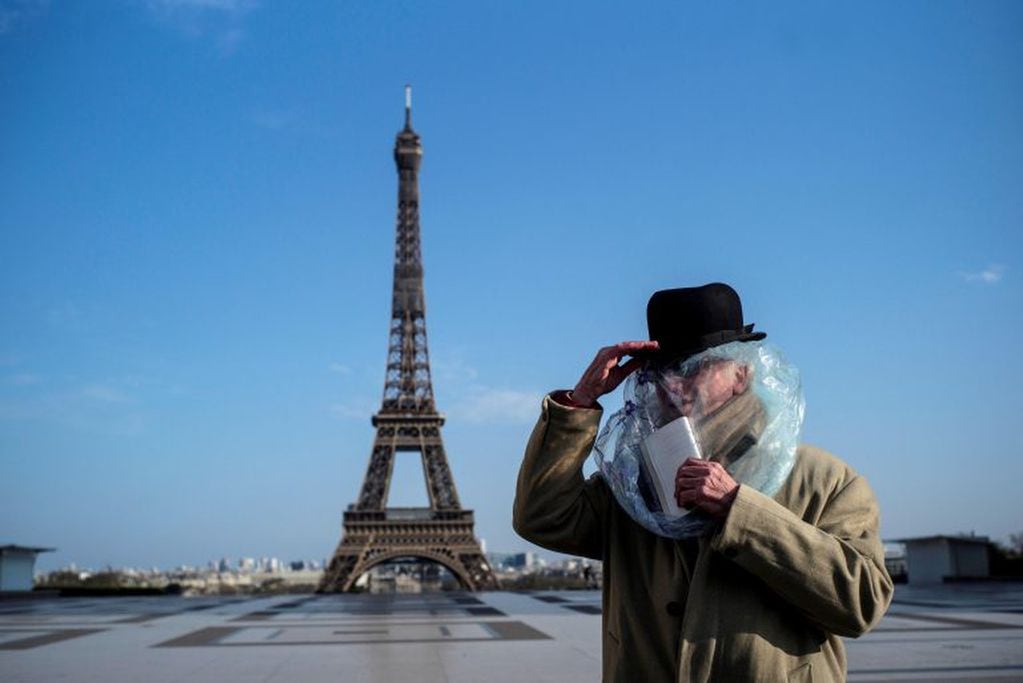 Un hombre cubierto con una bolsa de plástico lee un libro frente a la Torre Eiffel en París (Francia) (EFE/Julien de Rosa)