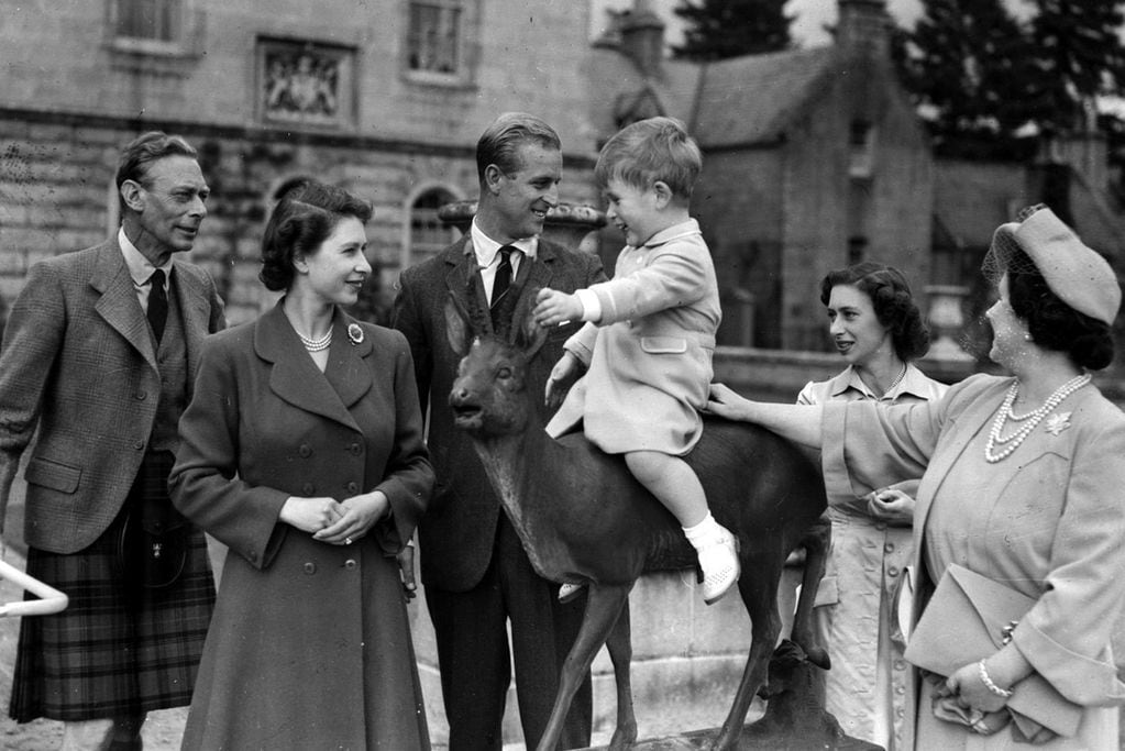 El príncipe Carlos de Gran Bretaña, vigilado desde la izquierda por el rey Jorge VI, la princesa Isabel, el príncipe Felipe, la princesa Margarita y la reina Isabel, en los terrenos del castillo de Balmoral, Escocia, en agosto de 1951.  (AP/ archivo)