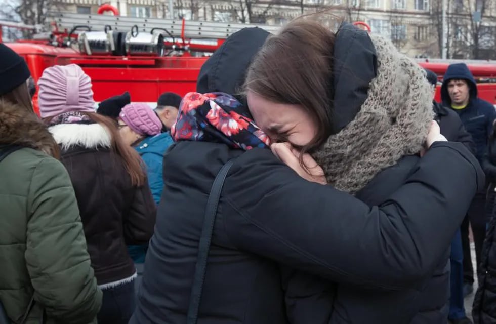 Dos jóvenes lloran junto al centro comercial incendiado en Rusia.