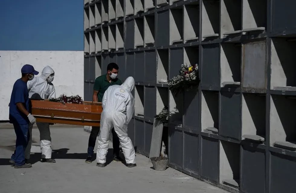 Cemetary workers wearing protective clothing place the coffin of a victim of the novel coronavirus, COVID-19, into a grave cubicle at Caju cemetary in Rio de Janeiro, Brazil, on May 9, 2020. - The novel coronavirus has killed at least 276,435 people worldwide since the outbreak first emerged in China last December, according to a tally from official sources compiled by AFP at 1900 GMT on Saturday. (Photo by Carl DE SOUZA / AFP)
