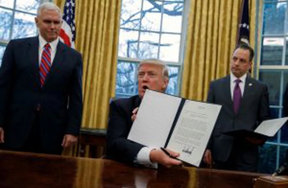 In this Jan. 23, 2017, photo, Vice President Mike Pence, left, and White House Chief of Staff Reince Priebus watch as President Donald Trump shows off an executive order to withdraw the U.S. from the 12-nation Trans-Pacific Partnership trade pact agreed t
