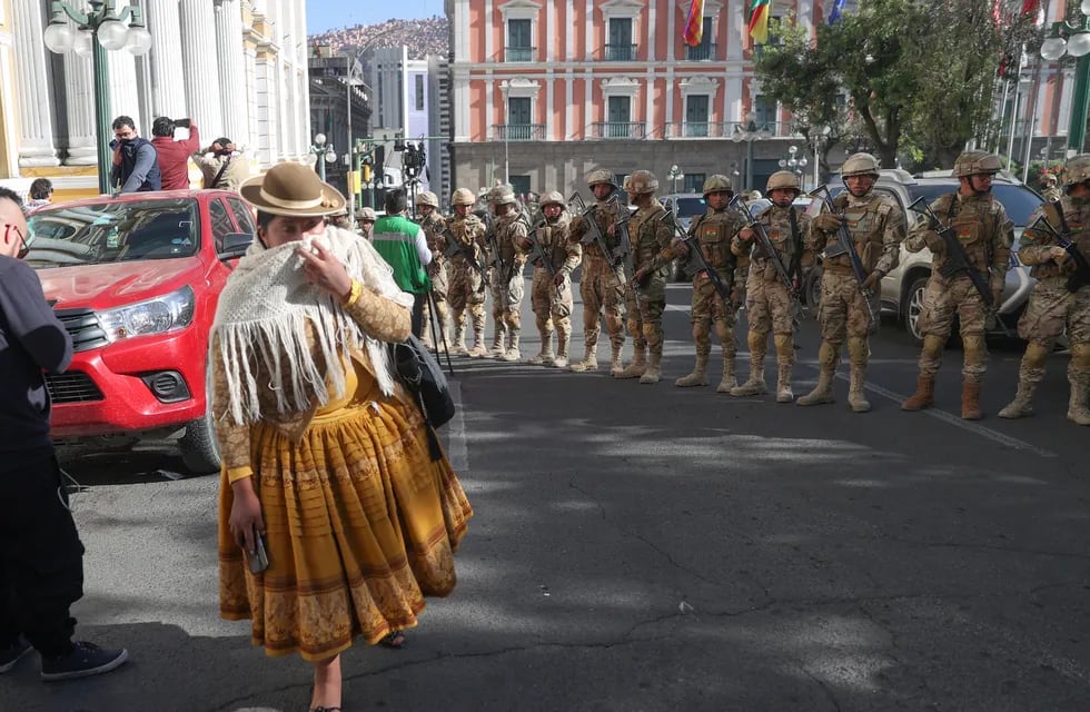 Una mujer pasa entre los militares formados frente a la sede del Gobierno de Bolivia, este miércoles en La Paz (Bolivia). El presidente Luis Arce dijo que el país "está atravesando un intento de golpe de Estado".