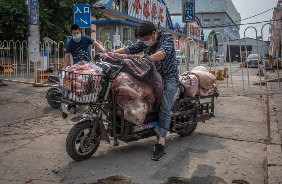 -FOTODELDÍA-PIL01. BEIJING, 13/06/2020.- Hombres con máscaras protectoras cargan un scooter con carne al lado del edificio cerrado del mercado Xinfadi en el distrito de Fengtai, Beijing, China, el 13 de junio de 2020. Uno de los mercados más grandes de Beijing, Xinfadi en el distrito de Fengtai, fue cerrado el 13 de junio, y el distrito colocado bajo bloqueo después de la confirmación de nuevos casos de coronavirus domésticos . EFE/EPA/ROMAN PILIPEY