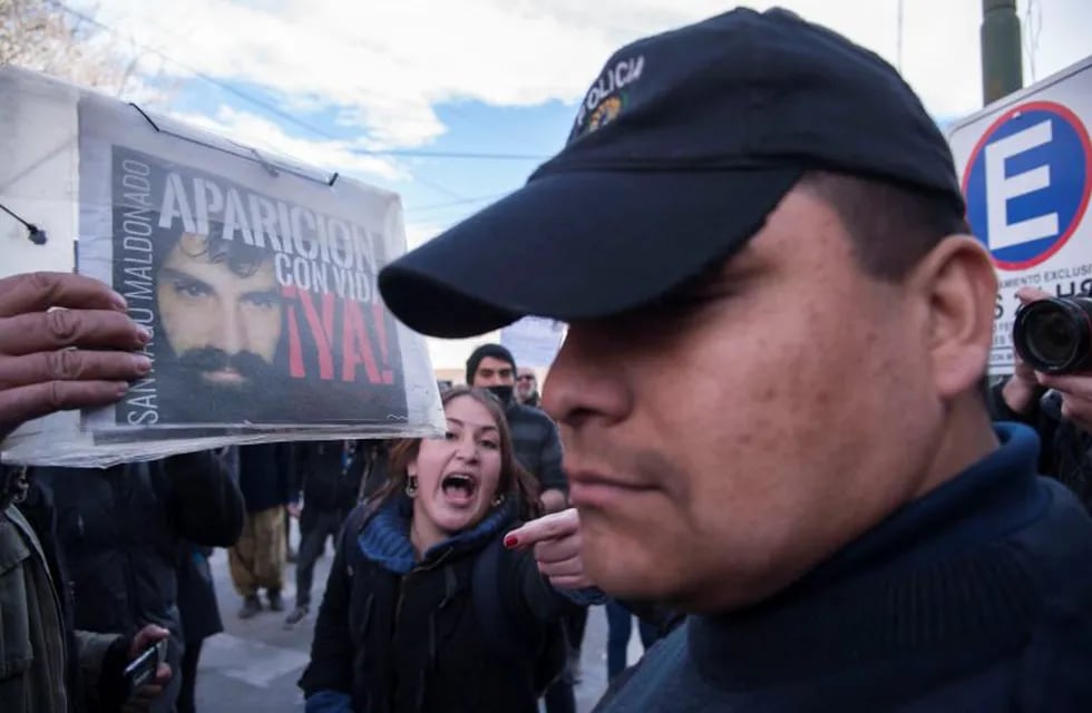 Un manifestante le muestra a un policía una foto de Santiago Maldonado durante una protesta frente a los Tribunales Federales de Esquel. Telam.