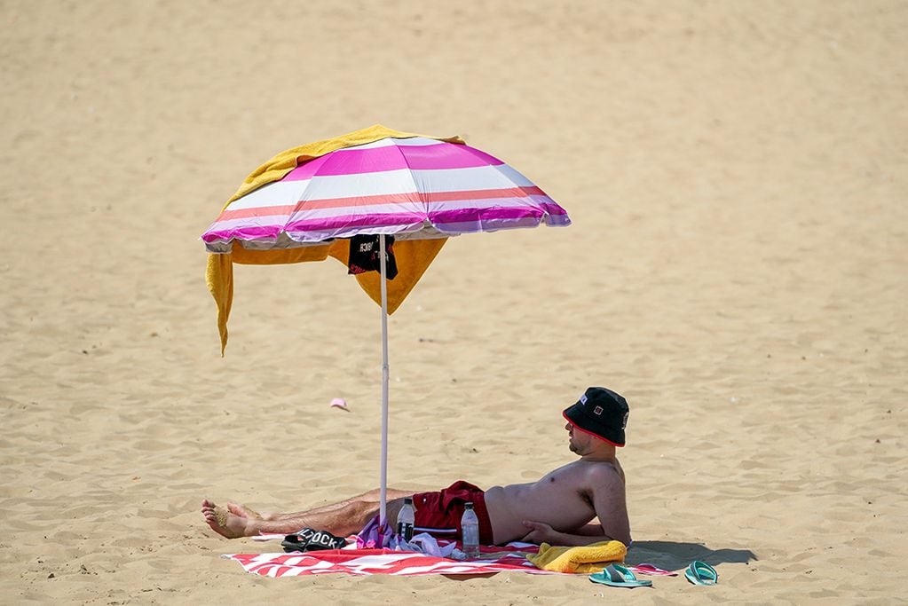 Un hombre se refugia bajo una sombrilla en la playa 