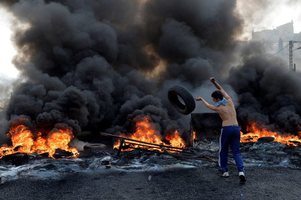 Un manifestante arroja una cubierta al fuego, en manifestaciones en las calles de Beirut, Líbano (EFE/EPA/WAEL HAMZEH)