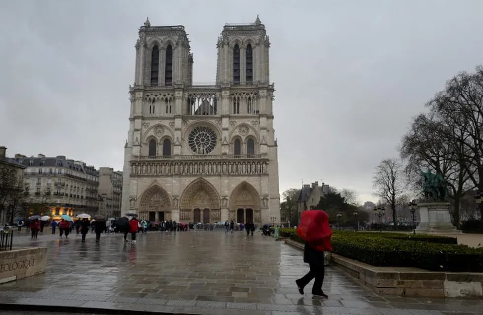 (FILES) In this file photo taken on March 29, 2018 a person walks in the rain in front of Notre-Dame de Paris Cathedral during the celebrations of Easter's Holy in Paris. - A fire broke out at the landmark Notre-Dame Cathedral in central Paris on April 15, 2019 afternoon, potentially involving renovation works being carried out at the site, the fire service said. (Photo by Ludovic MARIN / AFP)