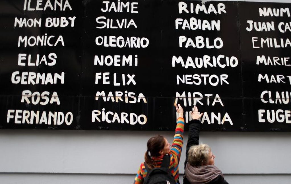 Women touch a board filled with the names of people who died in the bombing of the AMIA Jewish center, at the site of the attack 25 years ago in Buenos Aires, Argentina, Thursday, July 18, 2019. The bombing killed 85 people. (AP Photo/Natacha Pisarenko)