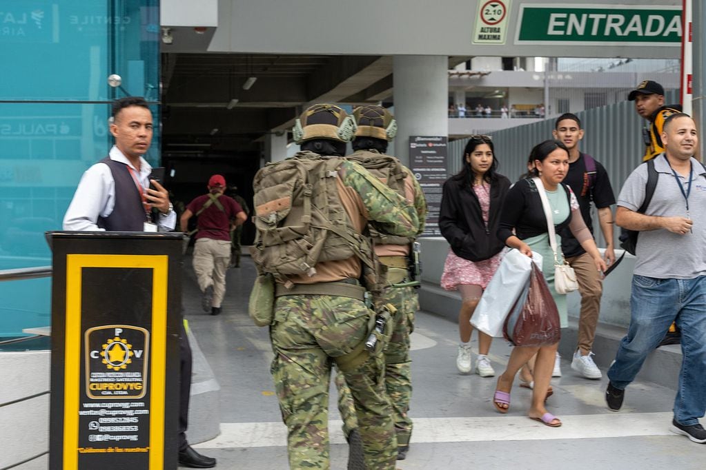 Soldados ecuatorianos persiguen este martes a un presunto delincuente mientras ciudadanos evacúan a pocas cuadras de la sede del canal de televisión TC, donde encapuchados armados ingresaron y sometieron a su personal durante una transmisión en vivo, en Guayaquil.