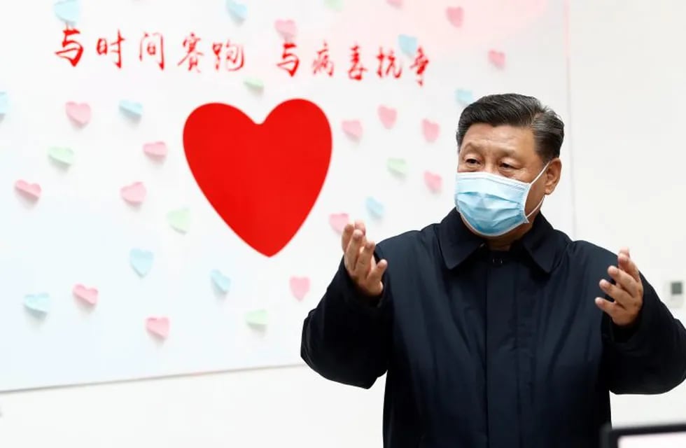 In this Feb. 10, 2020, photo released by Xinhua News Agency, Chinese President Xi Jinping gestures near a heart shape sign and the slogan \