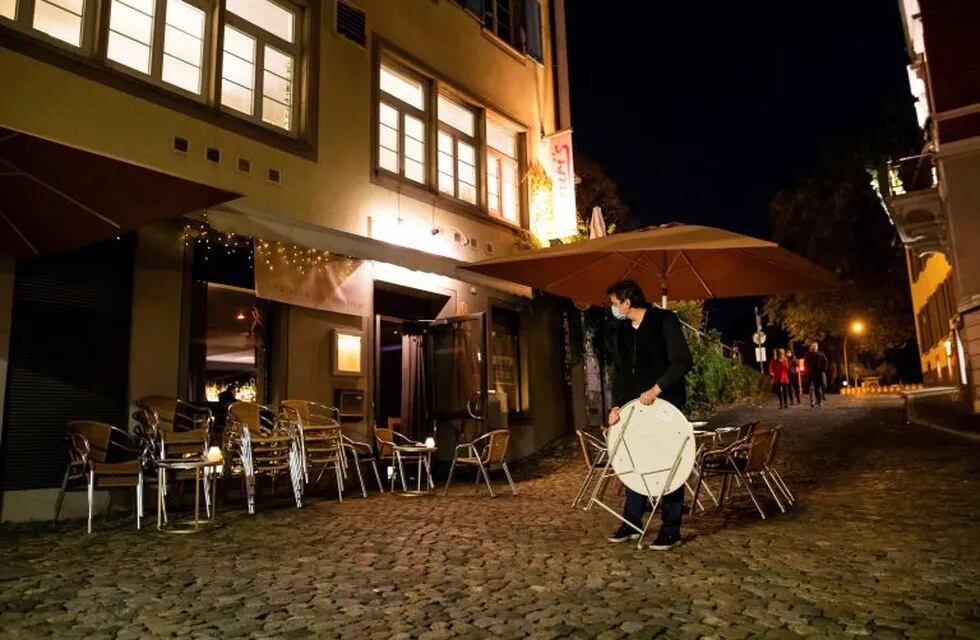 Shortly before closing time, the operator of a cocktail bar clears a table in the outdoor area at his bar in the city centre of Freiburg, Germany, on Friday, Oct. 30, 2020. He says he is desperate because of the upcoming measures that are set to take effect on Monday and last until the end of November. German officials have agreed to a four-week shutdown of restaurants, bars, cinemas, theaters and other leisure facilities in a bid to curb a sharp rise in coronavirus infections. (Philipp von Ditfurth/dpa via AP)