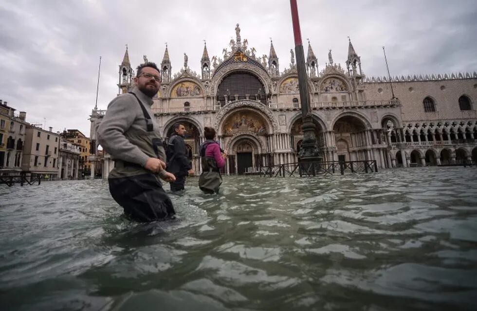 Una vista general muestra a personas caminando a través de la inundada Plaza de San Marcos, junto a la Basílica de San Marcos el 15 de noviembre de 2019 en Venecia, dos días después de que la ciudad sufriera su marea más alta en 50 años. Crédito: Filippo MONTEFORTE / AFP.