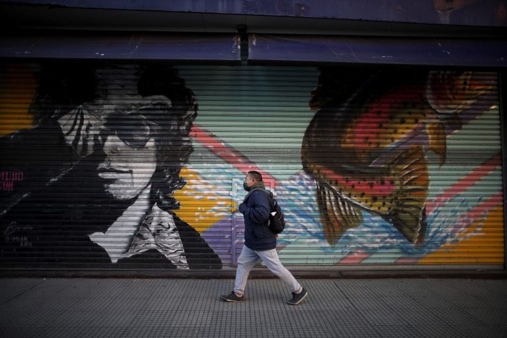 A man walks past a decorative roll-up storefront door amid the new coronavirus pandemic, in Buenos Aires, Argentina, Friday, June 26, 2020. Argentine President Alberto Fernandez is expected to announce a rollback on restrictions of the COVID-19 lockdowns in place since March 20th. (AP Photo/Natacha Pisarenko)