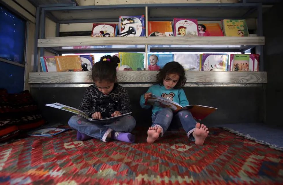In this Saturday, March 10, 2018 photo, Afghan children read books inside a bus library, in Kabul, Afghanistan. From sunrise to sunset, the bus drives around Kabul’s neighborhoods, stopping in each place for a couple of hours at a time. The mobile library was the initiative of 25-year-old Freshta Karim who wanted to give Kabul’s children something badly missing in her own childhood -- the chance to widen one’s horizons, free of the shadow of war and poverty. (AP Photo/Rahmat Gul) kabul afganistan  Charmaghz micro azul que pone contentos a los chicos afganos biblioteca sobre ruedas recorre los barrios de la capital afgana el omnibus lleva libros para que los chicos niños puedan leer