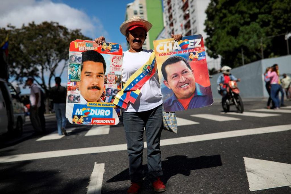 Una vendedora venezolana sostiene posters de Hugo Chávez y Nicolás Maduro (AP)